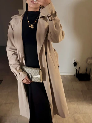 Beige trenchcoat med bälte - Lång beige trenchcoat med bälte. Använder aldrig den då den är i bra skick fortfarande ☺️skriv vid fler frågor/bild! 