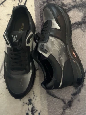 Louis Vuitton run away sneakers  - Snygga svarta sneakers från Louis Vuitton med refelx detaljer och klassisk LV-logga på plösen. Skorna har en chunky sula och är tillverkade i en mix av läder och textil. Perfekta för dig som vill ha en exklusiv och trendig look.