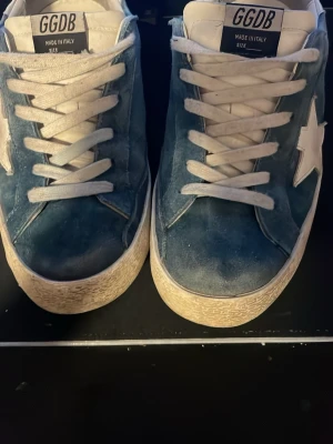 Golden gose skor snygga nu till sommarn  - Snygga blå sneakers från Golden Goose med vit stjärndetalj på sidan och vita skosnören. Ovandelen är i mocka och sulan är vit med en något ruffad look. Klassisk GGDB-tagg på plösen. Perfekta för en avslappnad streetstil. Ena skon är  Lite trasig men funkar perfekt det syns inte att dem är trasiga 