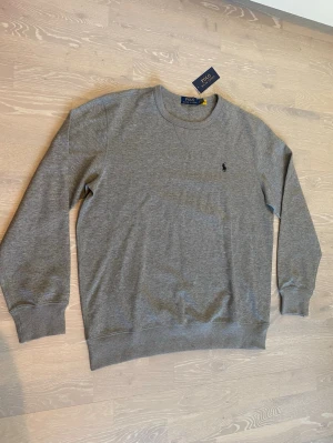 Grå sweatshirt från Polo Ralph Lauren - Hej! Säljer en stilren Grå Polo Ralph Lauren sweatshirt i Storlek L.                                                             Den är helt ny och har inga hål eller liknande.                       Som sagt är den i storlek L och måtten kan du se i sista bilderna 📐.                                                                    Priset kan diskuteras och jag skickar den inom 24 Tim 💨☺️