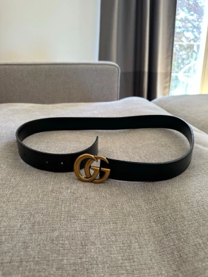 Svart skärp med GG-spänne - Snyggt svart skärp med klassiskt dubbelt GG-spänne i guld. Bältet har en stilren design som passar till många outfits. Perfekt accessoar för att lyfta din look.