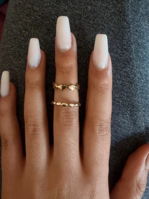 Två guldiga ringar med mönster - Säljer två tunna ringar i guldig metall med ett coolt geometriskt mönster runt om. Ringarna har en enkel men trendig design som passar perfekt att bära tillsammans eller var för sig. Perfekt accessoar för att lyfta din stil.