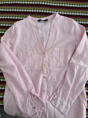 Ljusrosa Linneskjorta från Zara - Snygg ljusrosa skjorta från Zara i linne med v-ringning, knappar framtill och två bröstfickor. Perfekt för en avslappnad och trendig look. Långärmad modell med klassisk passform.