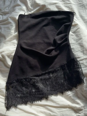 Spets topp Gina Tricot - Säljer en svart axelbandslös topp från Gina Tricot. Toppen har en snygg spetskant nertill som ger en extra touch. Perfekt för dig som gillar enkel men ändå elegant stil. Materialet känns mjukt och följsamt.