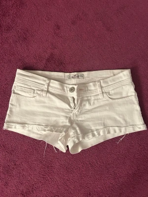 Vita denimshorts från Hollister - Snygga vita denimshorts från Hollister med låg midja. Femficksmodell med knapp och dragkedja framtill. Perfekta för varma sommardagar och enkel att matcha med allt.