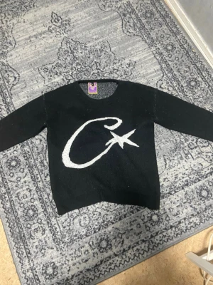 Svart stickad tröja med vit stjärna - Corteiz stickad tröja med c-stjärna på framsidan. Tröjan har rund halsringning och långa ärmar. Perfekt för dig som gillar unika och grafiska plagg. Materialet är mjukt och passar bra till många olika outfits. De står att den är M men skulle säga att den passar mer slm en L