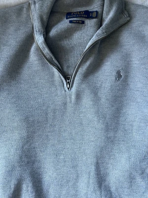 Grå  halvzip från Polo Ralph Lauren - Säljer nu denna snygga gråa halvzipen från ralph lauren, perfekt till en lite kallare dag, kan användas till alla olika stiler du kan tänka dig