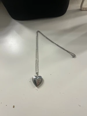 Silverfärgat hjärthalsband i metall, parfym - Snyggt halsband med ett hjärtformat hänge i silverfärgad metall. Kedjan är tunn och stilren, perfekt för att ge en romantisk touch till din outfit. Hjärtat har en blank yta och känns både trendigt och klassiskt. Med halsbandet medföljer två kuddar där du sprayar parfym så doften håller längre!!