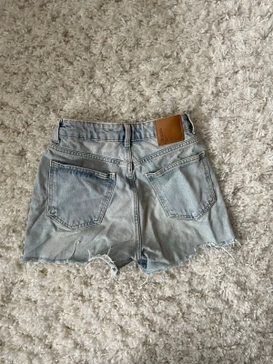 Levi's ljusblå denimshorts hög midja - Ljusblå denimshorts från Levi's med hög midja och fransiga benslut. Klassisk femficksmodell med knapp och dragkedja framtill samt läderpatch med logga bak.