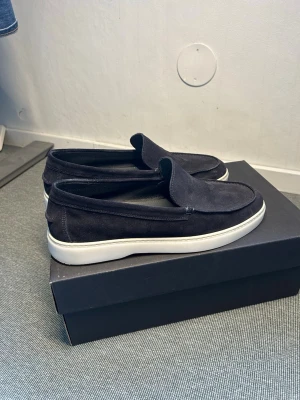 Svarta loafers från Massimo Dutti - Stilrena mörkblåa loafers i mocka från Massimo Dutti med vit sula. Skorna har en klassisk slip-on design och är perfekta för en avslappnad men snygg look. Materialet är mjukt och ger en lyxig känsla. Passar perfekt till jeans eller chinos.