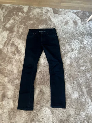 Svarta nudie jeans  - Snygga svarta slim jeans från nudie med klassisk femficksdesign och smal passform. Jeansen har normal midja och är tillverkade i stretchigt material för extra komfort. Perfekta för en trendig och stilren look.