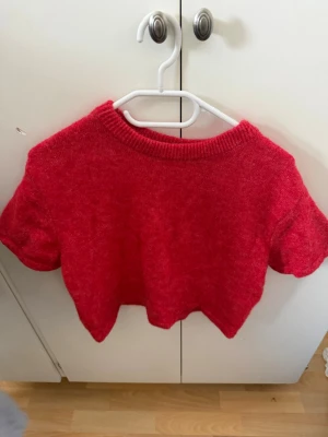Röd stickad kortärmad tröja Gina Tricot - Säljer en röd stickad tröja från Gina Tricot med korta ärmar och rund halsringning. Tröjan har en croppad passform och är gjord i ett mjukt, mysigt material. Perfekt för lager-på-lager eller som statement-plagg.