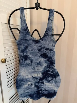 Blå batikmönstrad stickad klänning - Snygg stickad klänning i blått batikmönster med ärmlös design och rundad halsringning. Klänningen är kort och har en kroppsnära passform som framhäver siluetten. Perfekt för dig som gillar unika och trendiga plagg.