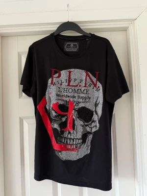 Svart t-shirt från Philipp Plein - Snygg svart t-shirt från Philipp Plein med glittrande detaljer och tryck framtill. T-shirten har rund halsringning och korta ärmar. Perfekt för dig som vill sticka ut med en exklusiv look.