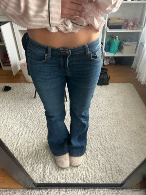 Blå bootcut jeans med låg midja - Snygga blå bootcut jeans med låg midja och klassiska fem fickor. Jeansen har en lätt utsvängd passform nertill och stängs med dragkedja och knapp. Perfekta för en avslappnad och trendig look.