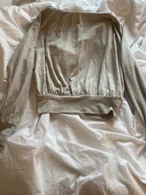 Ljusgrå croppad sweatshirt - Säljer en ljusgrå croppad sweatshirt med bred mudd i midjan och långa ärmar. Tröjan har en avslappnad passform och är tillverkad i mjukt material, perfekt för en chill och stilren look.