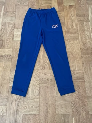 Blå Nike CR7 träningsbyxor  - Snygga blå träningsbyxor från Nike med CR7-logga på ena benet. Byxorna är tillverkade i Dri-FIT-material som andas och har resår i midjan med dragsko. 