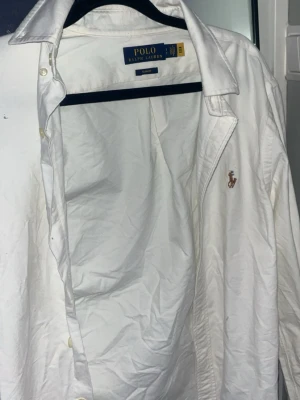 Vit slim fit skjorta Polo Ralph Lauren - Klassisk vit skjorta från Polo Ralph Lauren i slim fit-modell. Skjortan har långa ärmar, knappar framtill och den ikoniska broderade loggan på bröstet. Tillverkad i mjuk bomull för en clean och stilren look.