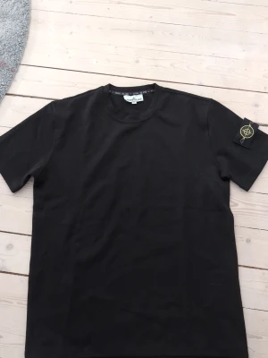 Svart Stone Island t-shirt - Xl men passar garanterat L (liten i storlek)Snygg svart t-shirt från Stone Island med klassisk logotyp-patch på ärmen. T-shirten har rund hals och korta ärmar, perfekt för en stilren och avslappnad look. Tillverkad i mjuk bomull som känns skön mot huden.