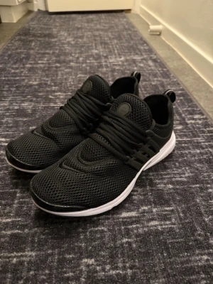 Svarta Nike Ultra Flyknit Air Prestos - Snygga svarta sneakers från Nike med ventilerande mesh-överdel och vita sulor. Skorna har en sportig look med svarta snören och diskret Nike-logga på sidan. Finns lite fläck på sidan av skorna. Perfekta för dig som gillar stilrena och bekväma sneakers till vardags.