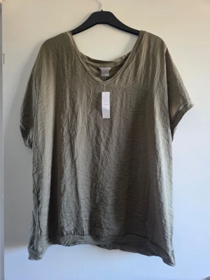 Olivgrön v-ringad linnetopp - Snygg olivgrön linnetopp från Zizzi med v-ringning och korta ärmar. Oversized passform som ger en avslappnad vibe. Perfekt att styla med jeans eller shorts för en chill look.