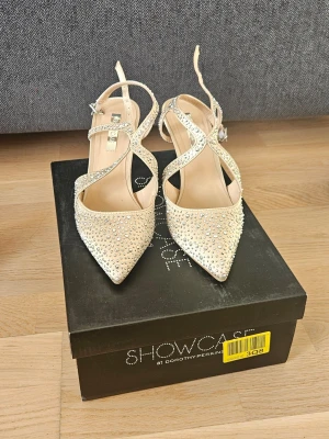 Glittriga pumps från Dorothy Perkins - Snygga pumps med spetsig tå och smala klackar från Dorothy Perkins. Skorna är ljusbeige med glittrande stenar och har eleganta korsade remmar med spänne. Perfekta för att sticka ut och ge outfiten extra bling.