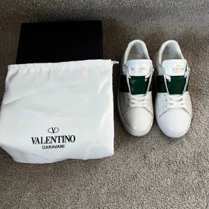 Valentino Garavani vita sneakers - Snygga vita sneakers från Valentino Garavani med gröna detaljer och klassisk logga på plösen. Skorna är låga och har en stilren design i läder, perfekta för dig som vill ha en exklusiv touch på din outfit.