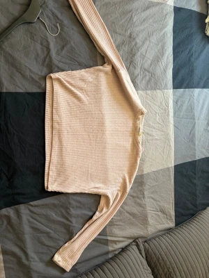 Ljusbeige ribbad långärmad tröja - Ljusbeige långärmad tröja med ribbad struktur och rund hals. Tröjan är mjuk och har en enkel, stilren design som passar perfekt till jeans eller kjol. Materialet ser ut att vara bomull eller en bomullsblandning. Perfekt för lager-på-lager under hösten.