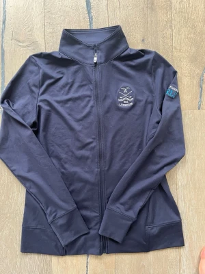 Marinblå ziptröja  från FJ - Svart ziptröja med hög krage och hel dragkedja. På bröstet finns ett broderat märke med texten 'LJUNGHUSEN' och på ärmen står det 'Team Future GIRLS' i vitt och turkost🌸💗