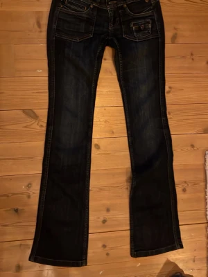 Mörkblå bootcut jeans Freeman T Porter - Snygga mörkblå lågmidjade bootcut jeans från Freeman T Porter med kontrastsömmar och flera fickor fram. Klassisk femficksmodell i slitstarkt denimtyg. Perfekta för dig som gillar en avslappnad men ändå trendig look.