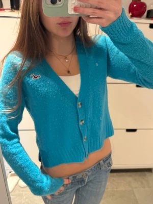 Ljusblå hollister stickad kofta - Klarblå stickad Hollister-kofta med knappar! Storlek S! Bra skick, men förvänta dig ett litet fel (sista bilden)! Har Hollisters fågellogga på bröstet och små slitsar på sidorna. Följ för fler liknande kläder och köp bundle!