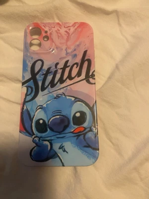 Stitch mobilskal med rosa och blått - Snyggt mobilskal med motiv av Stitch från Disney. Skalet har en färgglad design i rosa och blå toner med texten 'Stitch' i svart. Tillverkat i tålig plast och passar perfekt för dig som vill ha ett unikt och lekfullt mobilskal.