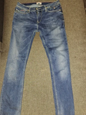 Blå slim fit jeans från Hilfiger - Säljer ett par blå slim fit jeans från Hilfiger Denim med klassisk femficksmodell och snygga slitningar. Jeansen har ljus tvätt, raka ben och Hilfiger-lapp bak i midjan. Perfekta till en avslappnad stil och passar till det mesta.