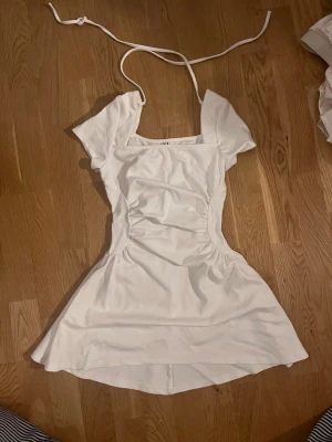 Vit kortklänning från Y6Y - Supersöt vit kortklänning från Y6Y med puffärmar och smickrande rynkade detaljer längs sidorna. Klänningen har en fyrkantig ringning och knytband i nacken för en extra fin touch. Perfekt för sommarens alla tillfällen!