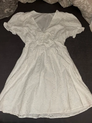 Vit kort klänning med broderi - Söt vit kortklänning med v-ringning och puffiga kortärmar. Klänningen har fina broderade detaljer och volang vid ärmslutet. Perfekt för sommarens alla tillfällen och ger en romantisk känsla. Lappen där bak är klippt och har använt 1 gång!