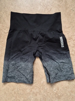 Gymshark bike shorts - Korta, thighta, högmidjade gymshark shorts i svart med grå gradient. Fint skick, loggorna är hela.
