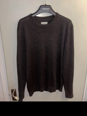 Grå merinoulltröja These Glory Day(Volt) - Grå med lätt brun färg stickad tröja från These Glory Days i mjuk superior merinoull. Klassisk rund halsringning och ribbade muddar vid ärmslut och nederkant. Perfekt för lager på lager och enkel att matcha med olika stilar.