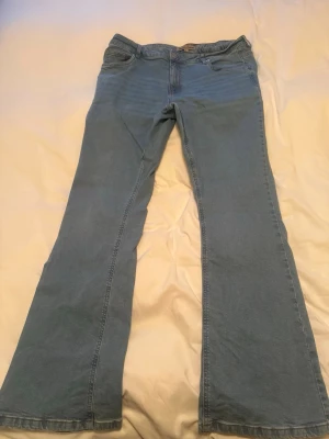 Ljusblå bootcut jeans - Säljer ett par ljusblå bootcut jeans med klassiska fem fickor och dragkedja. Jeansen har en utsvängd passform från knäna och är tillverkade i denim. Perfekt för dig som gillar retrostil och vill ha ett avslappnat men trendigt plagg.