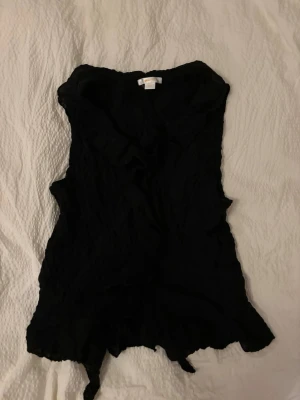 Svart volangblus - Säljer en svart blus från med volangdetaljer och v-ringning. Blusen är ärmlös och har en våfflad struktur. Den är i storlek 170 men för mig som har S i damstorlek sitter den perfekt. Verkligen så fin och söt!!