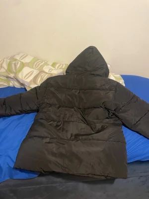 Svart moncler jacka - PRISET KAN DISKUTERAS!! Snygg svart dunjacka från Moncler med huva och klassisk Moncler-logga på ärmen. Jackan har en puffig design och är tillverkad i glansigt material som ger en modern look. Perfekt för kalla vinterdagar. 