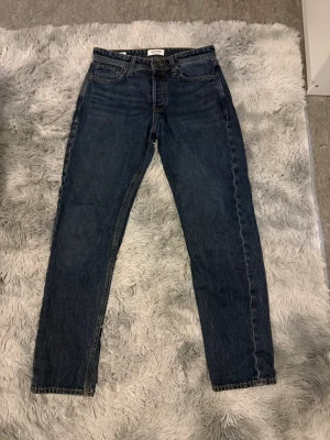 Mörkblå relaxed jeans från Jack and Jones  - Säljer ett par mörkblå jeans från Weekday med rak passform och hög midja. Klassisk femficksmodell med knappgylf och läderpatch bak i midjan. Jeansen är tillverkade i kraftig denim och har en tidlös look.