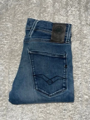 Replay Anbass jeans - Mörka blåa Replay Anbass jeans. Midja 34cm, längd 99cm. Obs jeansen har en lite reva på vänster smalben, och ett hål vid skrevet som har stygn över sig. JAG SKICKAR EJ FLER BILDER NÄR JAG BÄR JEANSEN! för bättre inblick i passformen rekommenderar jag att googla på modellnamnet. För storleksguide kolla måtten noggrant då jeansen alltid kan vara uppsydda heller krympta och jag ej tar emot returer :) 1,63