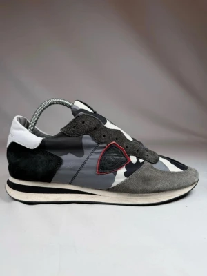 Philippe Model TRPZ - Snygga sneakers från Philippe Model med grå, svart och vit camo-mönstrad textil, grå mockadetaljer och svart samt vit häl. Röd detaljsöm runt loggan på sidan. Skön och modern design som sticker ut. Storlek 42 men passar 43