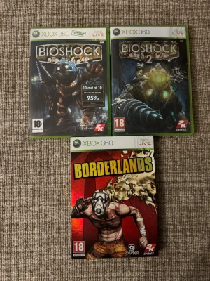 Xbox 360 spel: BioShock & Borderlands - Tre Xbox 360-spel: BioShock, BioShock 2 och Borderlands. Alla i sina originalfodral med snygga omslag. BioShock-spelen har mörka, futuristiska motiv medan Borderlands har en röd, tecknad stil. Perfekt för dig som gillar action och äventyr.