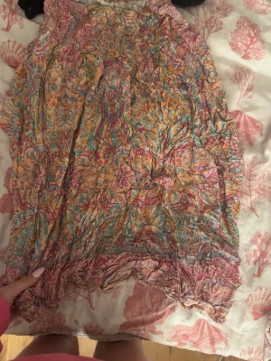 Färgglad mönstrad kjol från Marta - Säljer en färgglad kortkjol från Marta med blommigt mönster i rosa, orange, blått och gult. Kjolen har resår i midjan och är gjord i ett lätt och luftigt material, perfekt för varma dagar. Passar dig som gillar boho-stil och vill ha något unikt i garderoben.