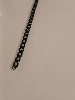Svart kedjehalsband i metall - Snyggt svart halsband med grova länkar i metall. Kedjan har en karbinhake som lås och en enkel, stilren design som passar till många olika looks. Perfekt för dig som gillar en edgy och modern stil.