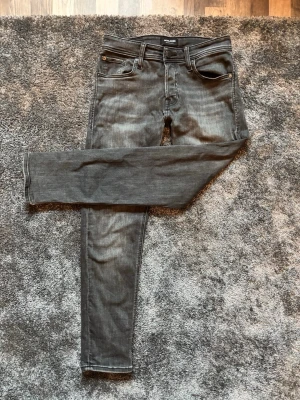 Grå slim fit jeans från jacknjones - Säljer ett par gråa slim fit jeans från Jack n Jones med klassisk femficksmodell och svarta sömmar. Jeansen har en något tvättad look och är tillverkade i stretchigt denimtyg för skön fit