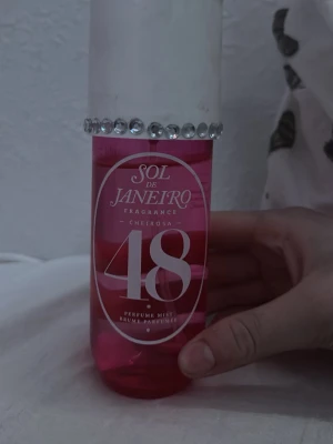 Sol de Janeiro Cheirosa 48 Perfume Mist - Sol de Janeiro Cheirosa 48 Perfume Mist i en rosa plastflaska med vita detaljer och en dekorativ rad av glittrande stenar runt korken. Flaskan har en modern, rundad form och tydlig logga framtill.