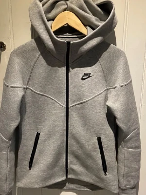 Grå zip hoodie från Nike - Snygg grå hoodie från Nike med dragkedja framtill och svart Nike-logga på bröstet. köpt för 1300 säljer för 500kr i storlek S dam pris kan diskuteras #nike   