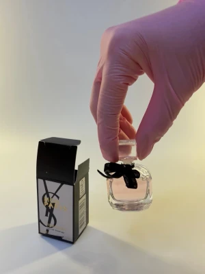 Yves Saint Laurent Mon Paris parfym 7,5 ml - Säljer en elegant Mon Paris Eau de Parfum från Yves Saint Laurent. Flaskan är liten, genomskinlig och fylld med ljusrosa parfym, dekorerad med en svart rosett runt halsen. Kommer i en snygg svart och silver kartong med guldtext. Perfekt för dig som gillar lyxiga dofter.